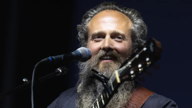 Sam Beam of Iron and Wine smiling at the microphone with an acoustic guitar