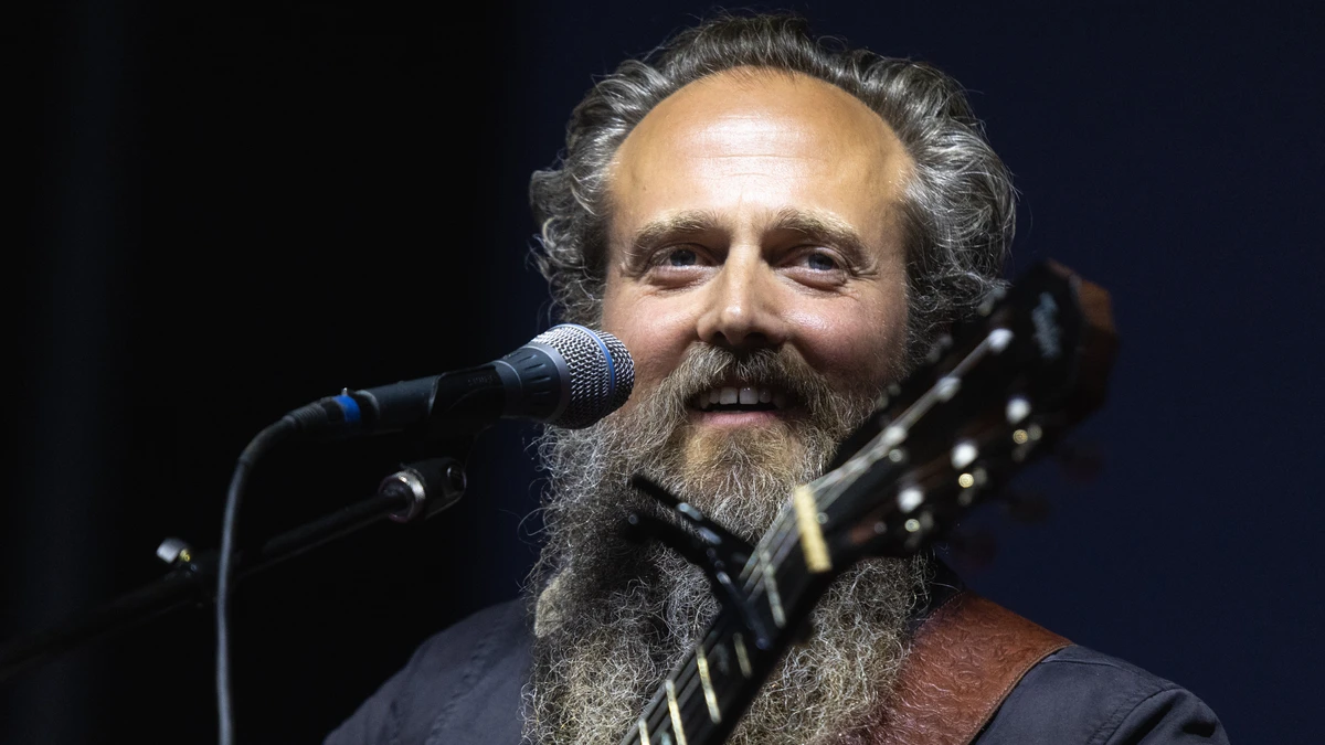 Sam Beam of Iron and Wine smiling at the microphone with an acoustic guitar