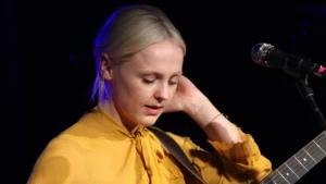 Laura Marling with an acoustic guitar at the microphone in a mustard blouse