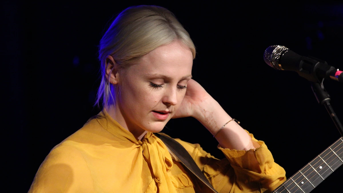 Laura Marling with an acoustic guitar at the microphone in a mustard blouse